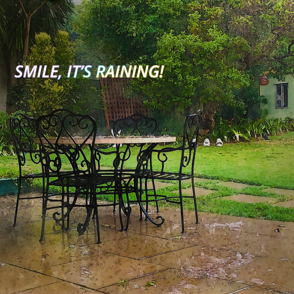 Rain falling on an outdoor garden patio with iron chairs and lush green lawn